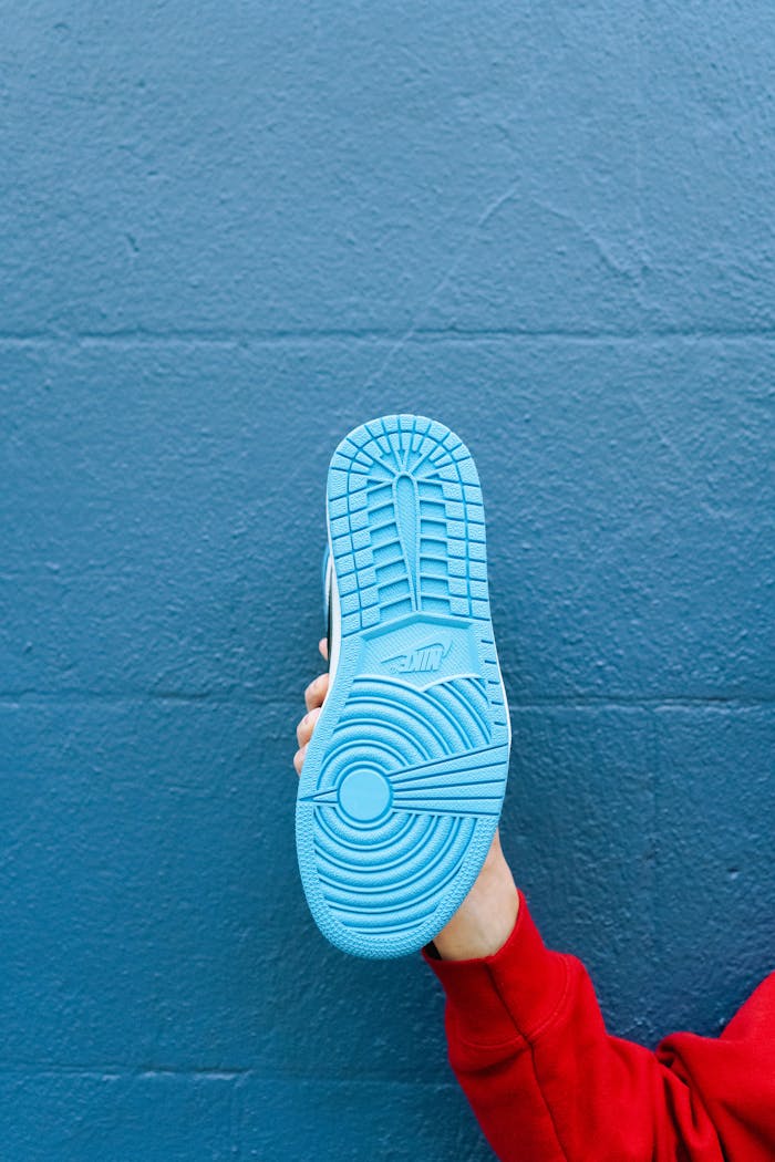 A vibrant blue sneaker sole held by a hand against a textured blue wall background.